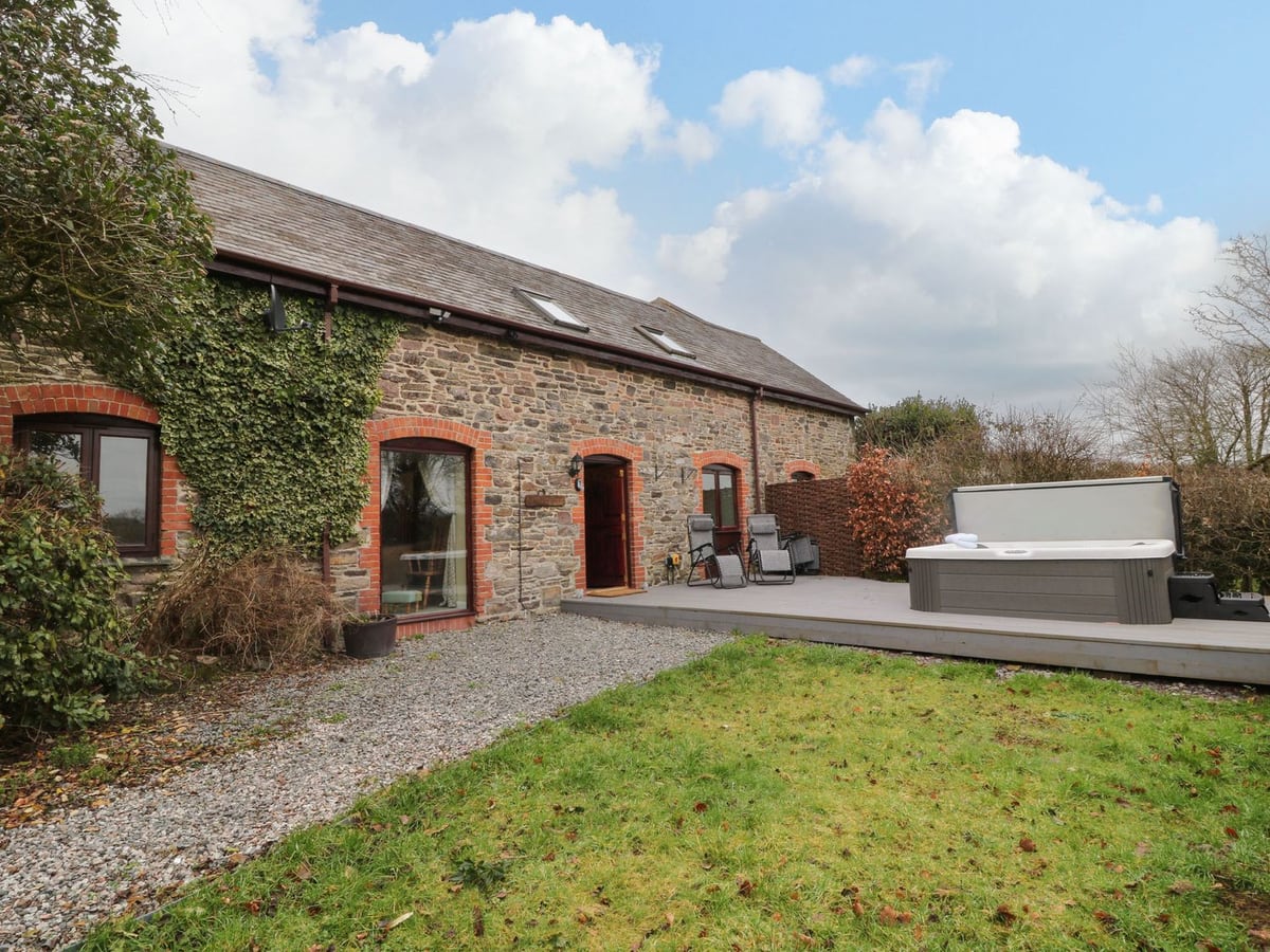 Stone facade beside a lawn, gravel path and deck with a hot tub at The Hawthorns