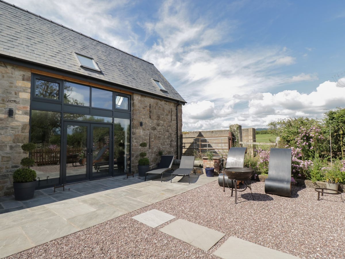 The Hay Barn opening onto a paved and gravelled patio with four loungers and a metal fire pit
