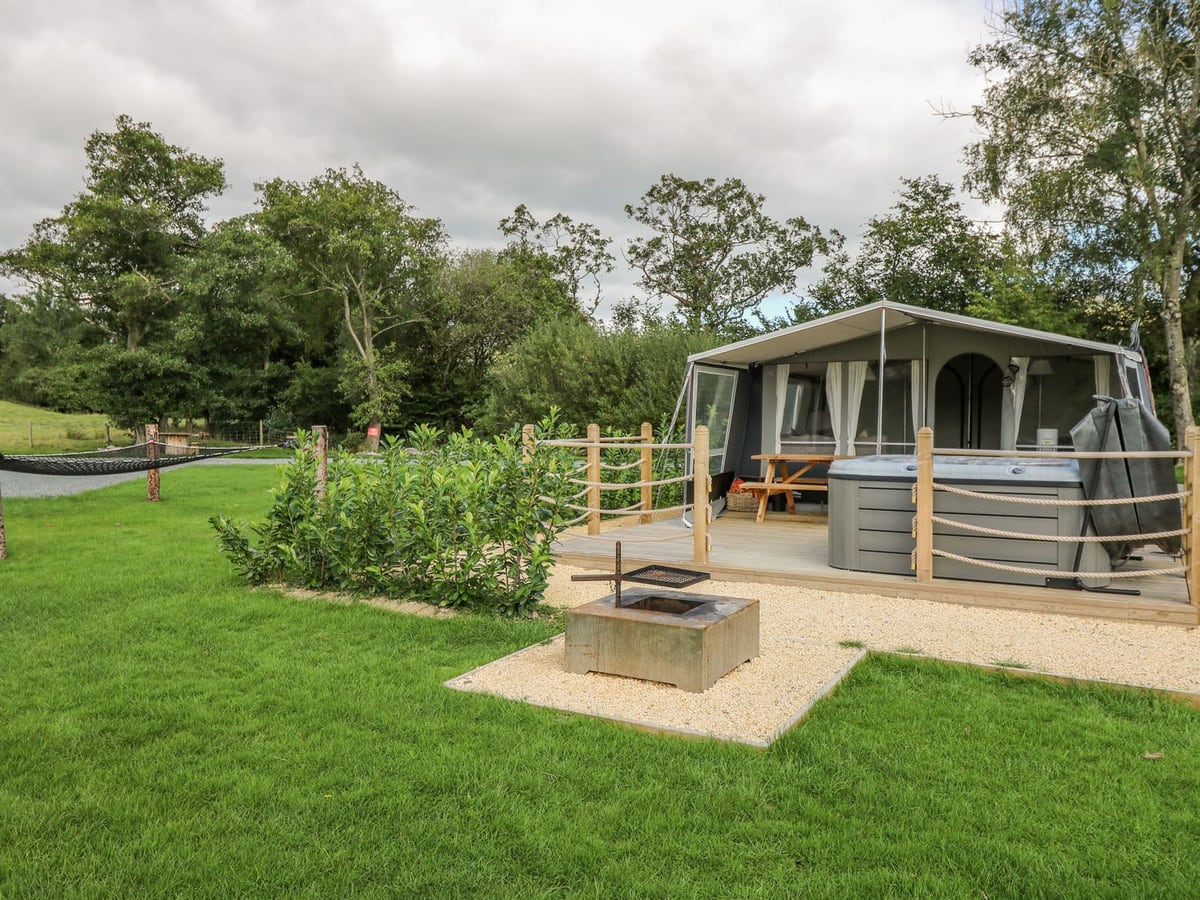 The Heron glamping tent with a rope-railed deck, hot tub, picnic bench and a fire pit on the lawn