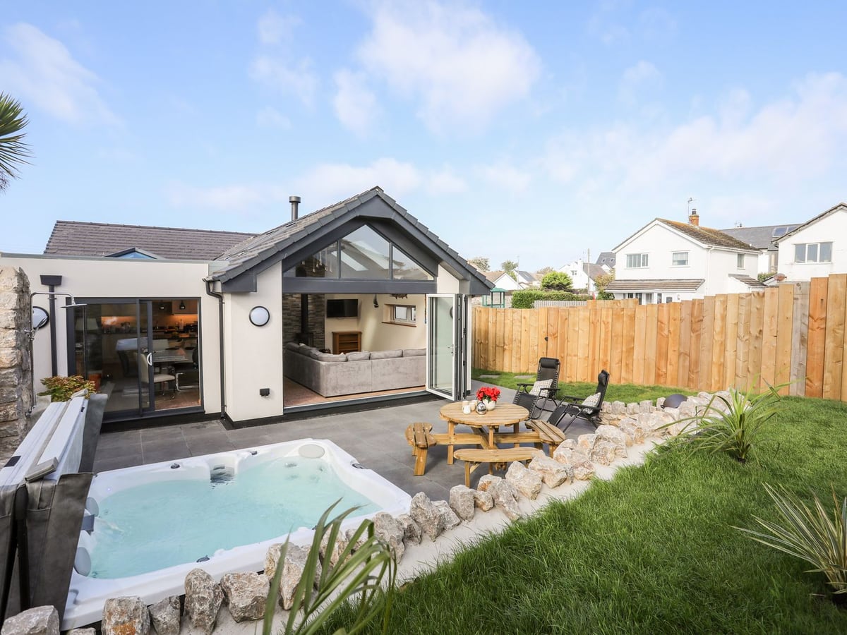 The Herun rear garden with lawn, patio seating and a hot tub beside open living-room doors