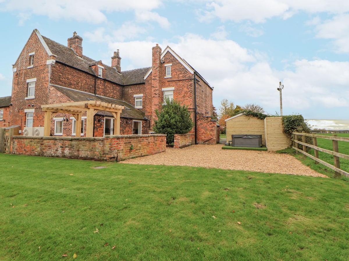 Lawn, red-brick farmhouse and covered hot tub at The House at School Farm