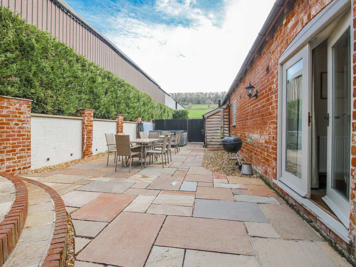 The Milking Parlour's paved patio with dining seats, brick steps and a hot tub at the far end