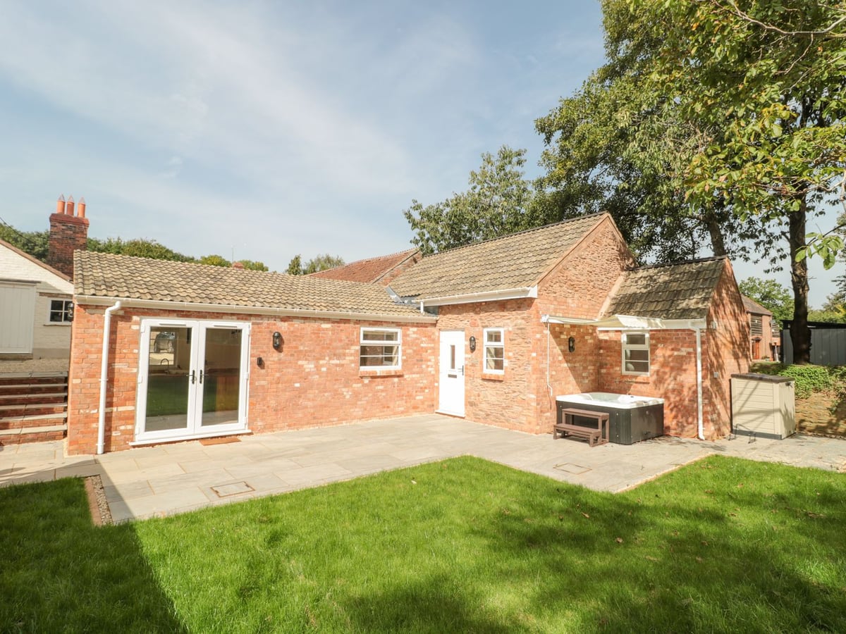The Nest lawn and patio with hot tub outside the single-storey brick cottage