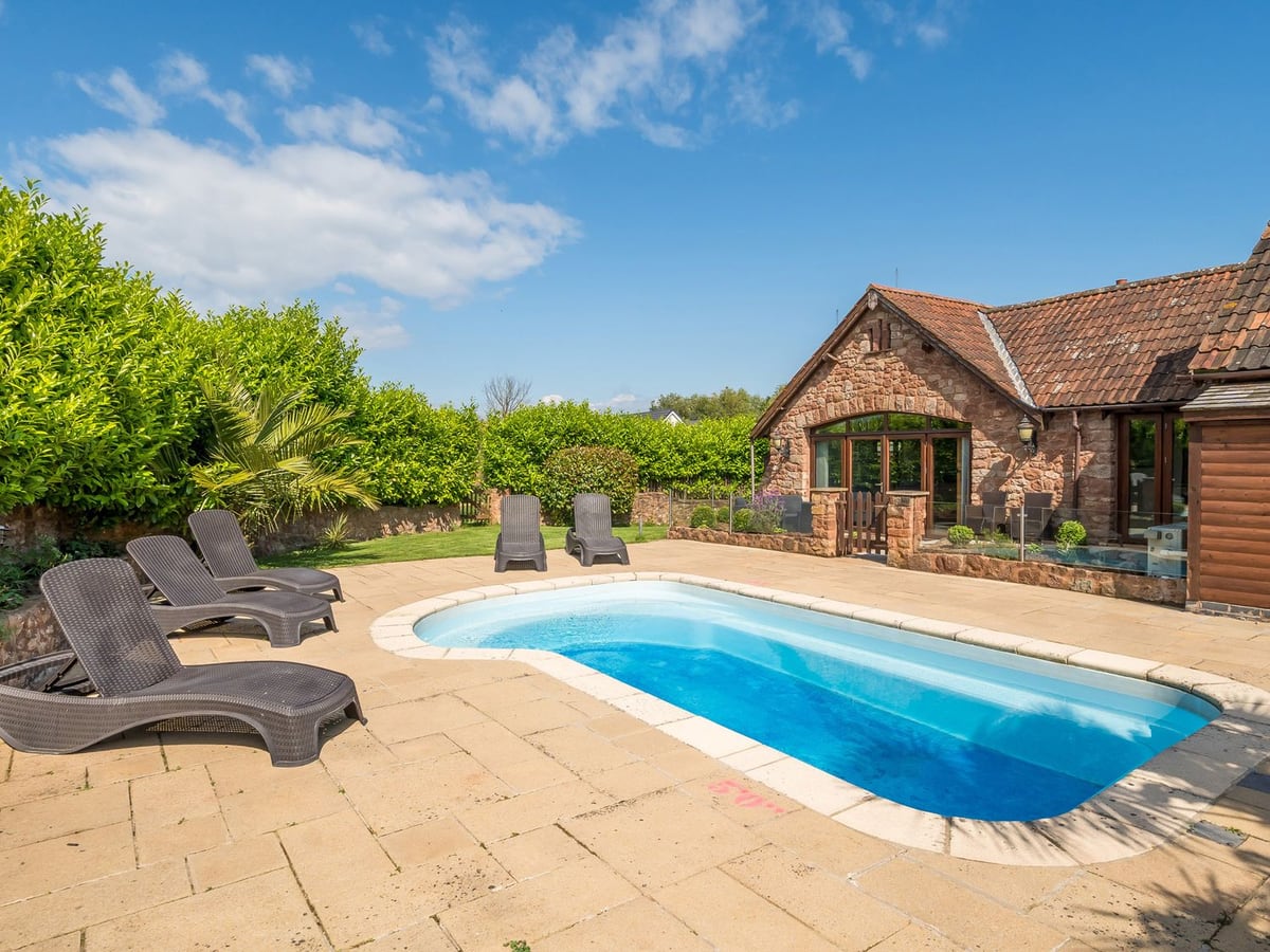 The Old Byres outdoor pool with lounge chairs and patio beside the stone house