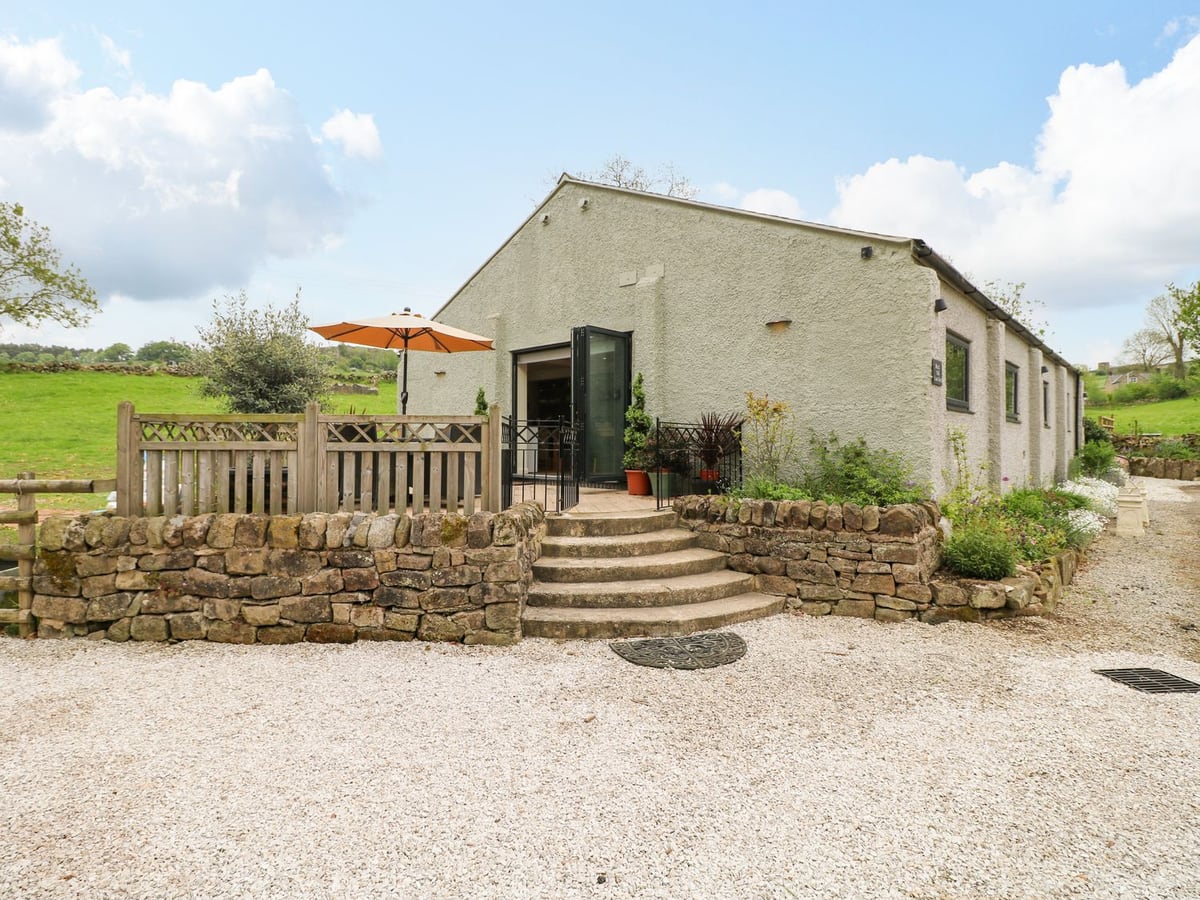 The Old Cowsheds with a raised terrace, orange parasol, stone steps and gravel approach
