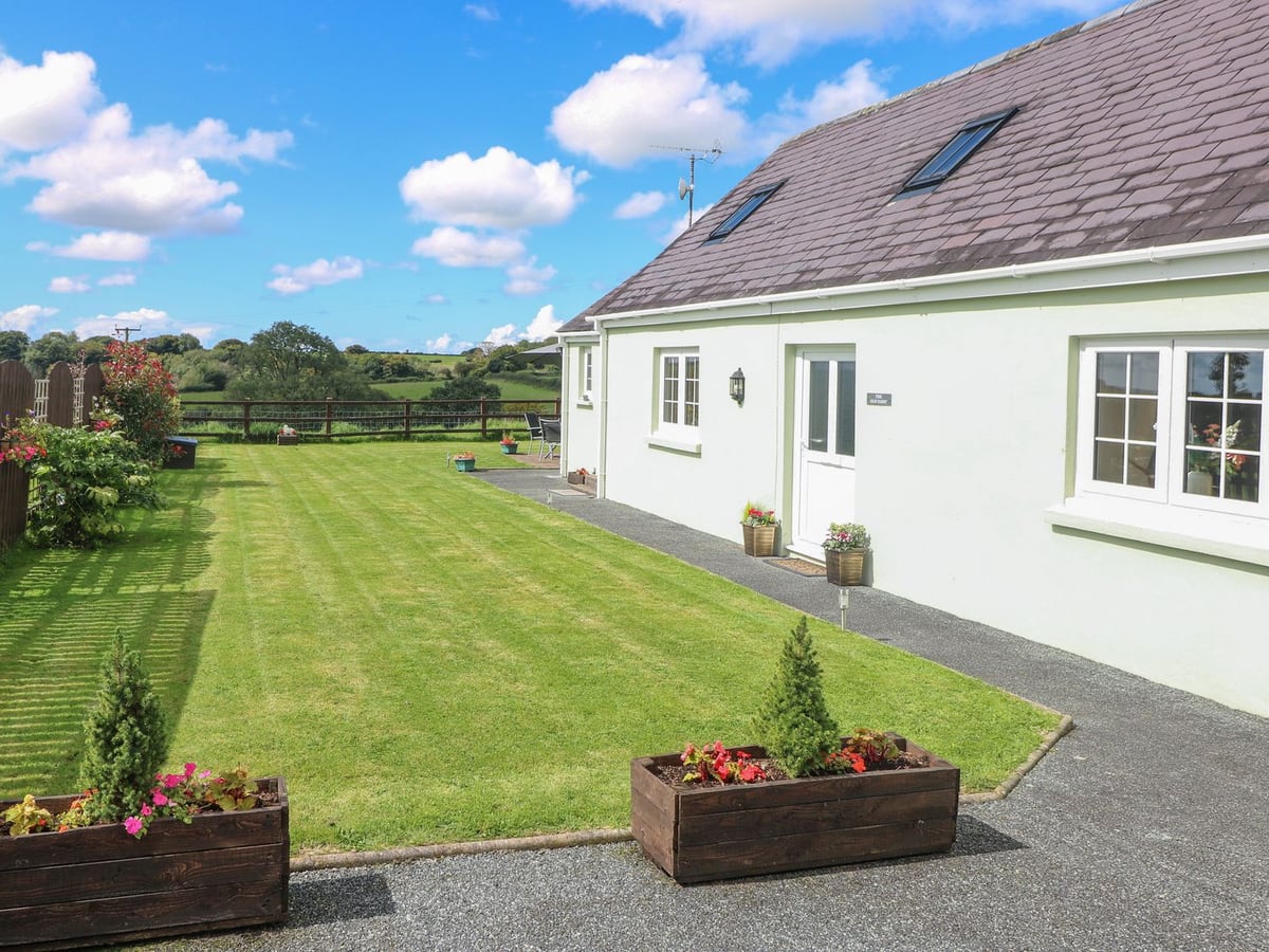 The Old Dairy cottage beside a long mown lawn with a timber rail fence and green fields beyond