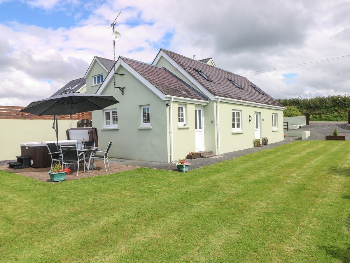The Old Dairy with a lawn, hot tub and shaded dining table beside the pale green cottage