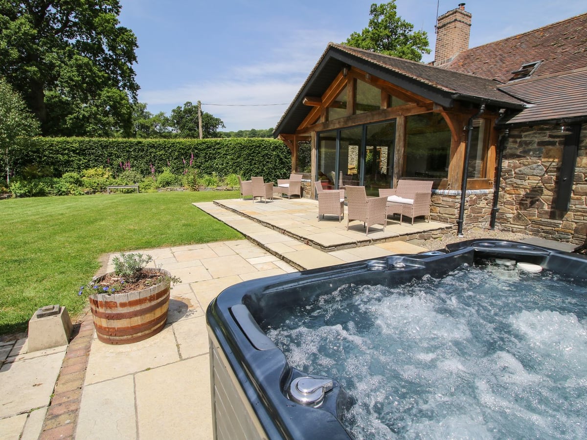 The Old Farmhouse's hot tub beside lawn, stone paving and a glazed timber extension