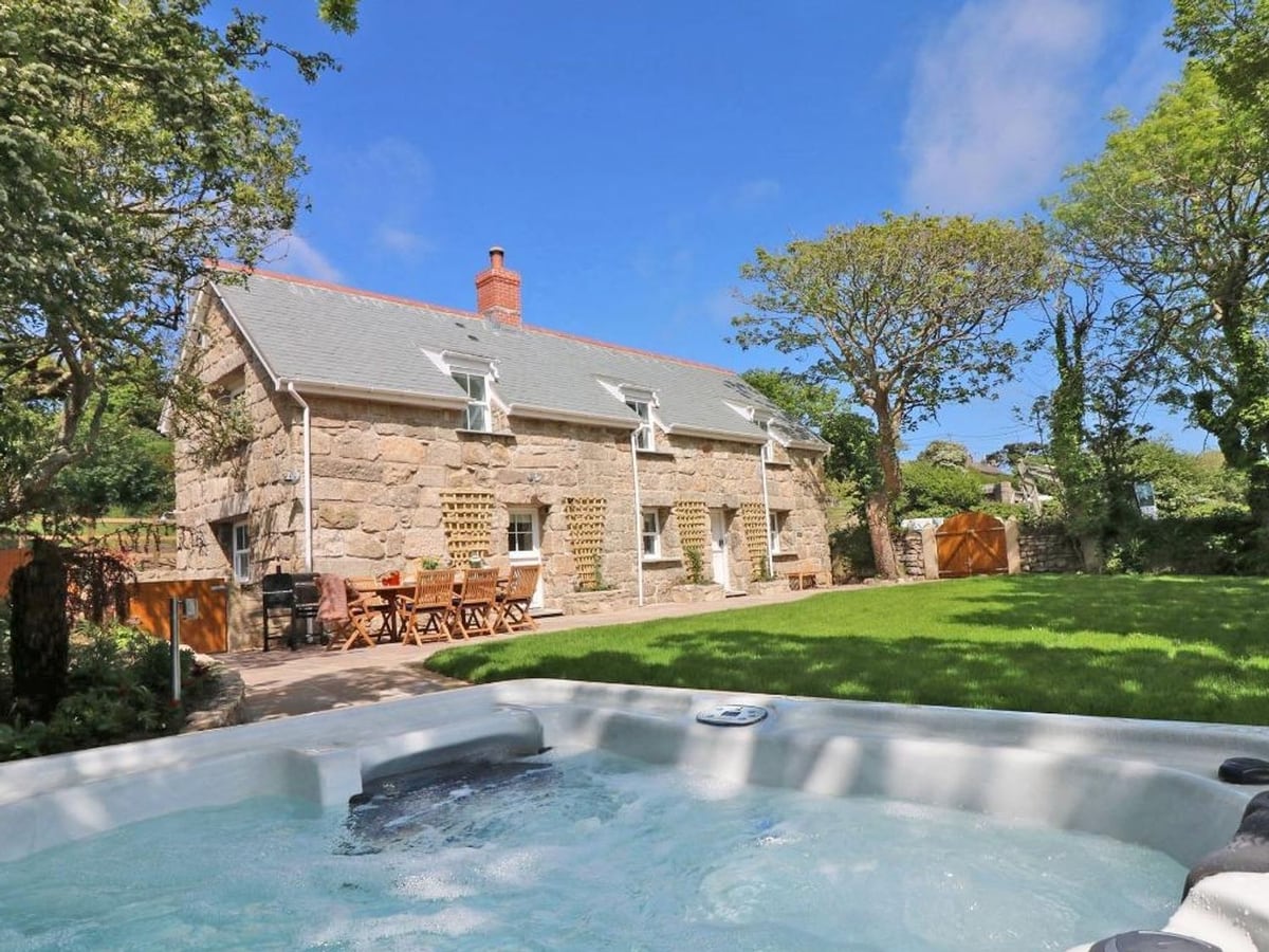 Hot tub overlooking the lawn, stone cottage and outdoor dining table at The Old Forge, St Just