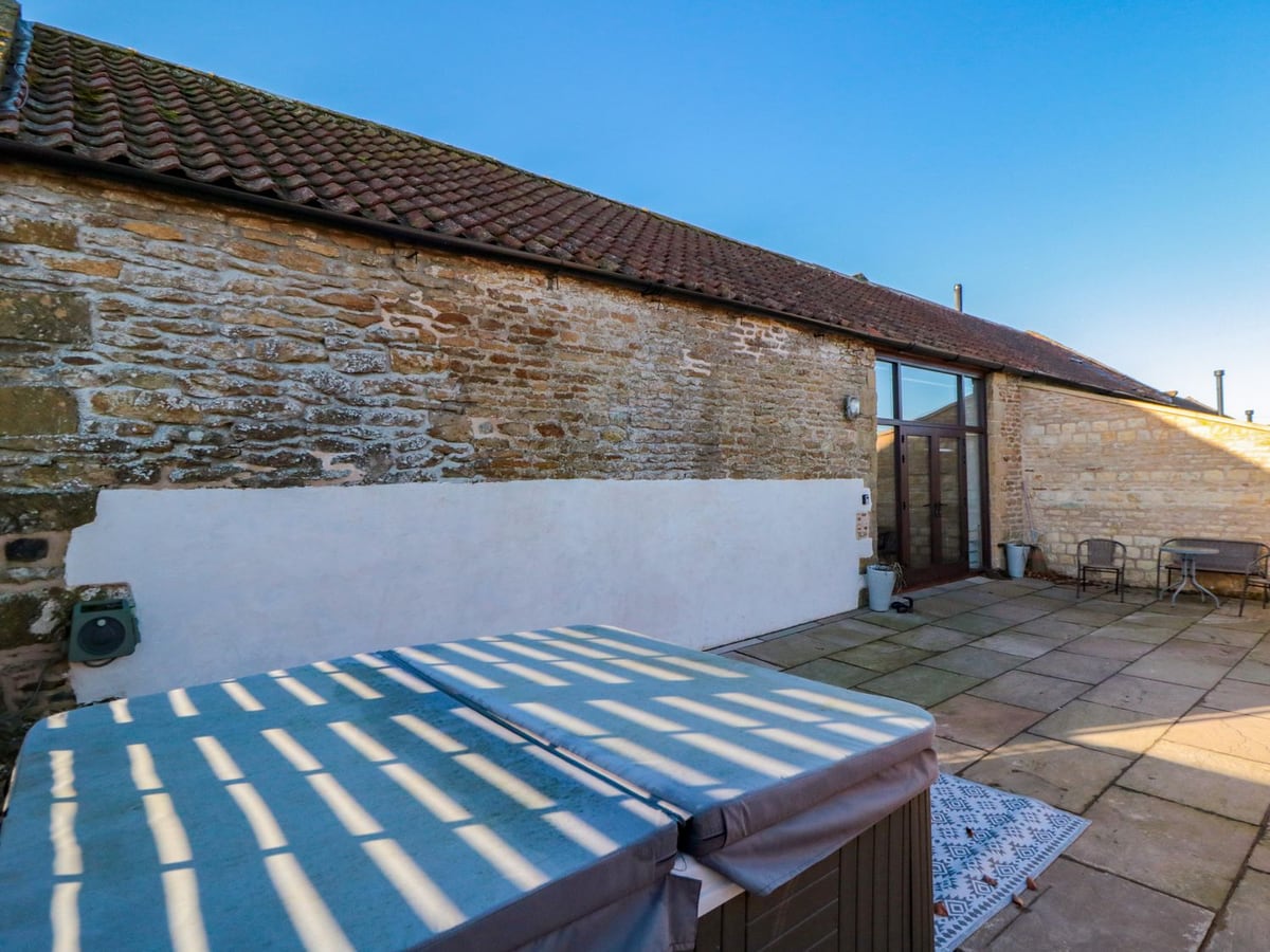 Stone courtyard with covered hot tub and outdoor seating at The Old Workshop