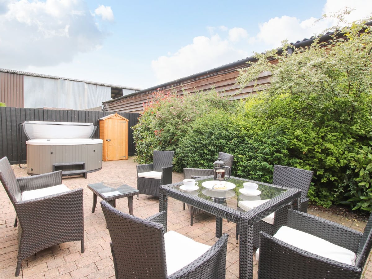 The Olde Cowshed's brick-paved courtyard with outdoor chairs and a pale round hot tub