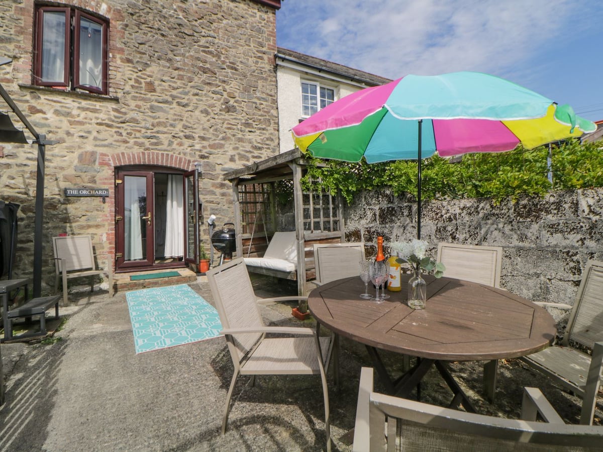 Stone courtyard with a dining table and colourful parasol beside The Orchard cottage