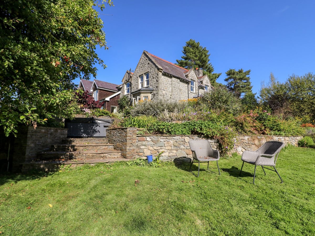 Lawn with two garden chairs below stone terraces, a covered hot tub and The Pheasantry behind