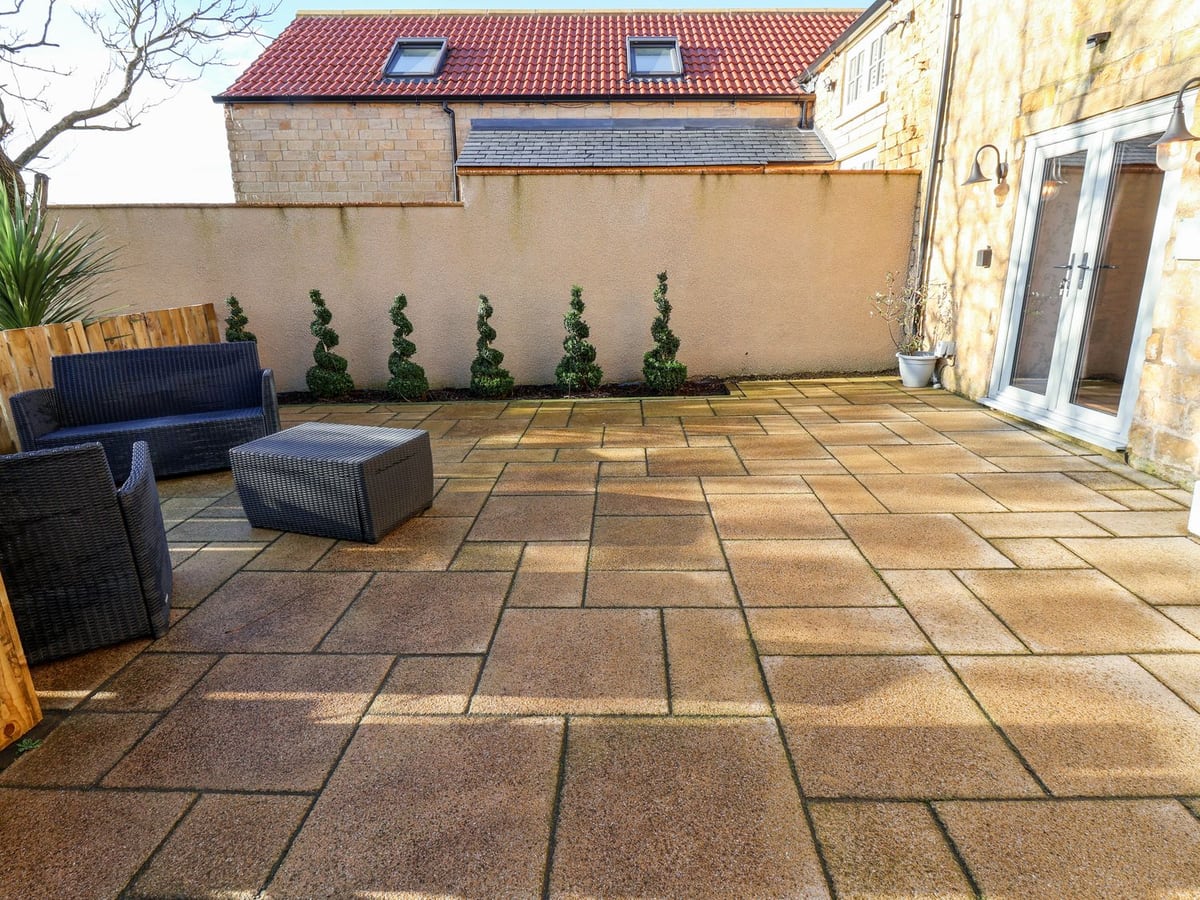 Paved courtyard with dark outdoor seating beside the stone exterior of The Pheasantry