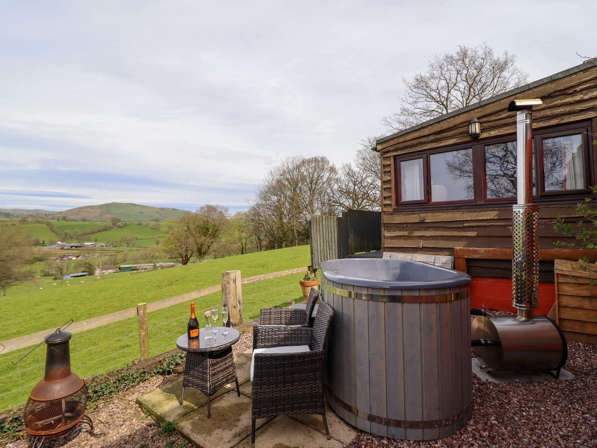 The Retreat timber cabin with a wood-fired hot tub, patio seating and a fenced field view