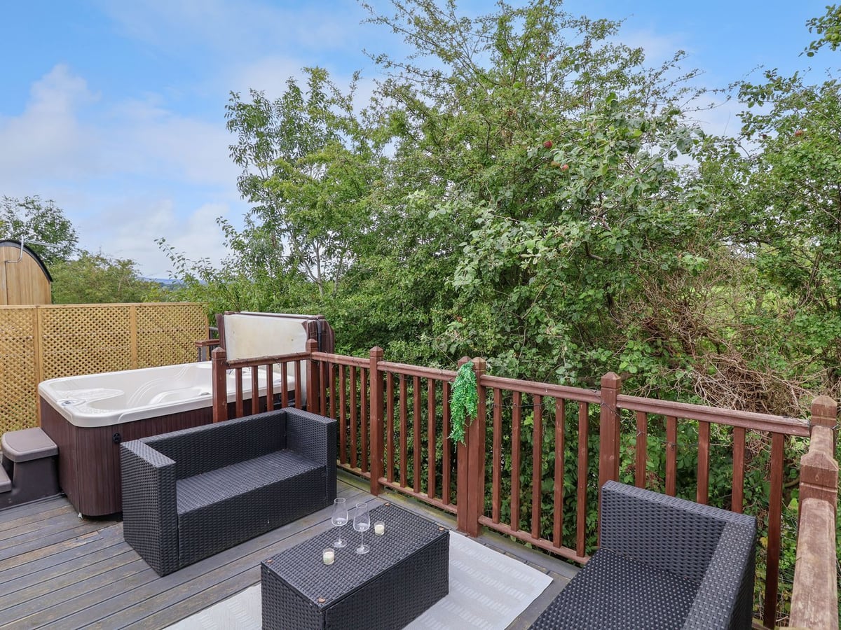 The Retreat railed deck with rattan seating and a hot tub with its lid raised, beside trees