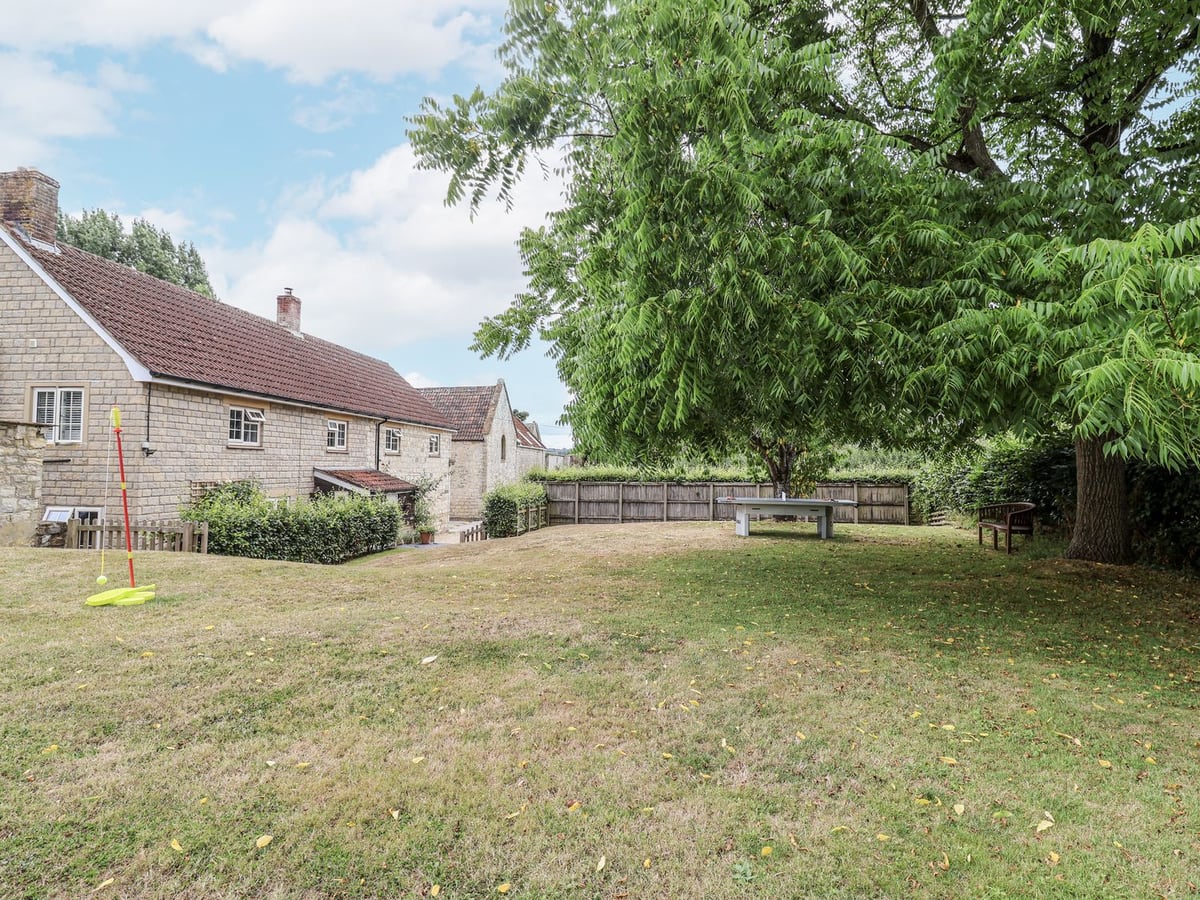 Lawn, mature tree and table tennis table behind the stone exterior of The Stable House