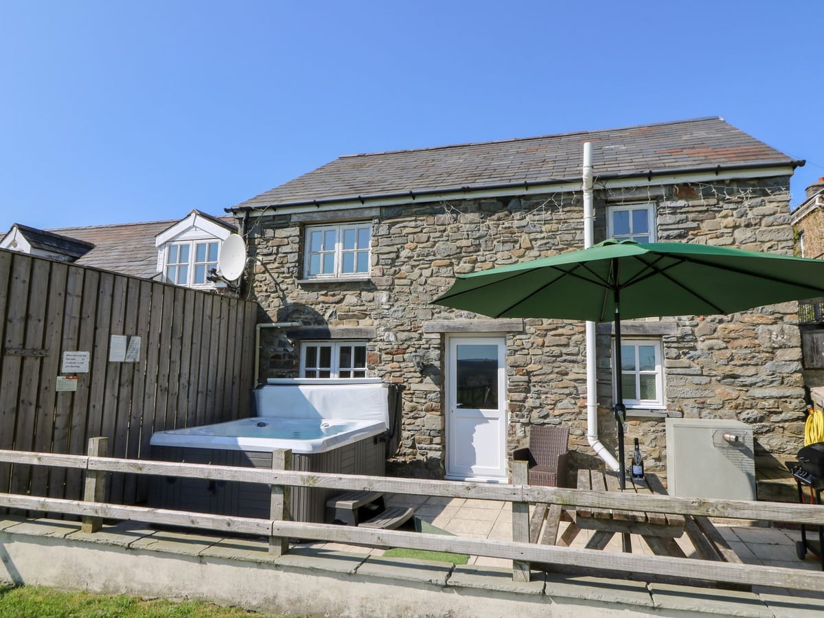 The Stable stone cottage with a hot tub, picnic bench and green parasol on a patio behind a low rail fence
