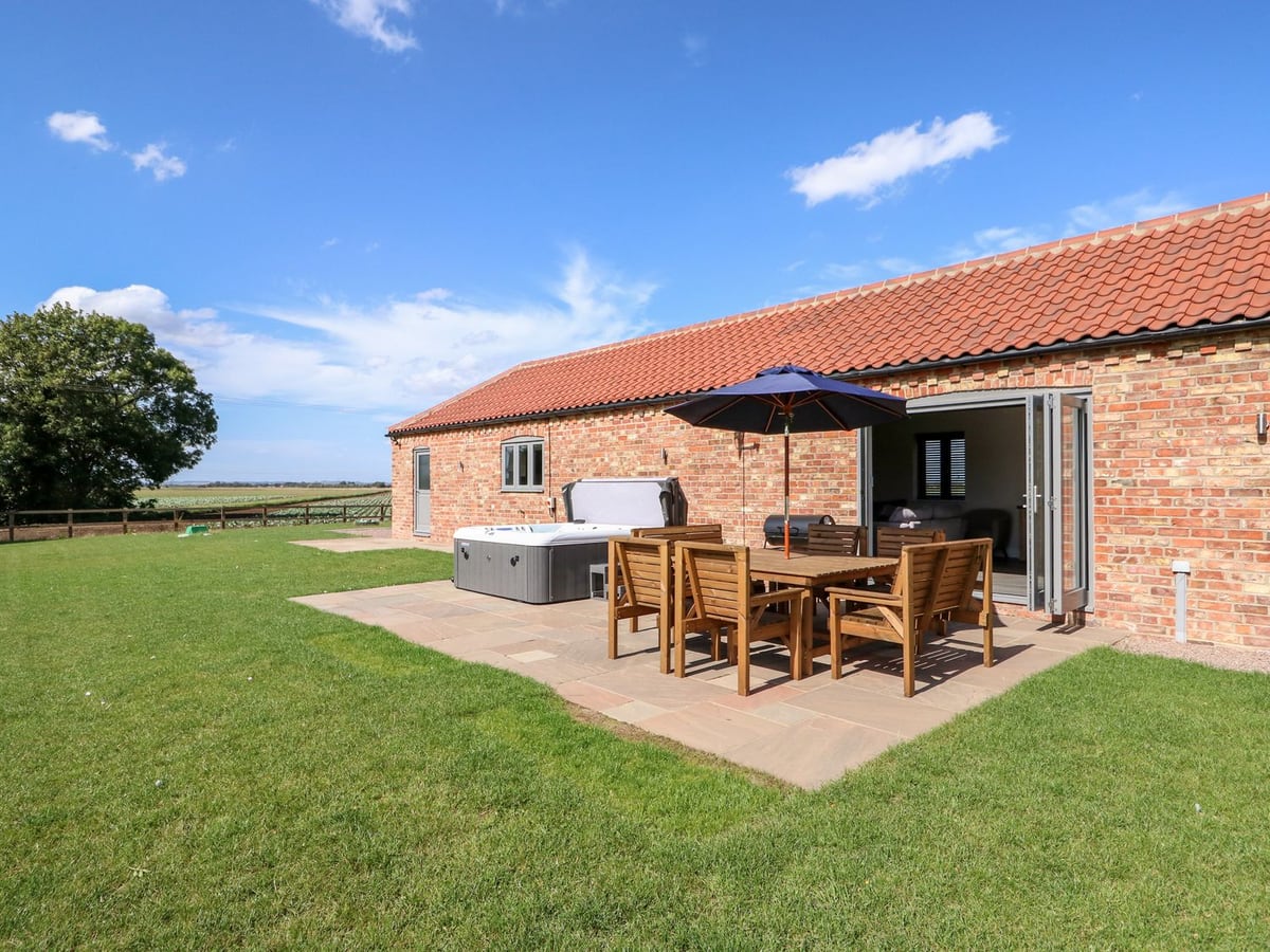 The Stables' brick exterior beside a lawn and patio with dining furniture and hot tub