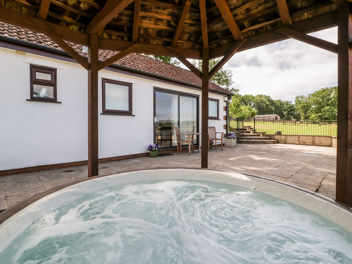 The Stables covered hot tub on the patio beside the cottage and fields