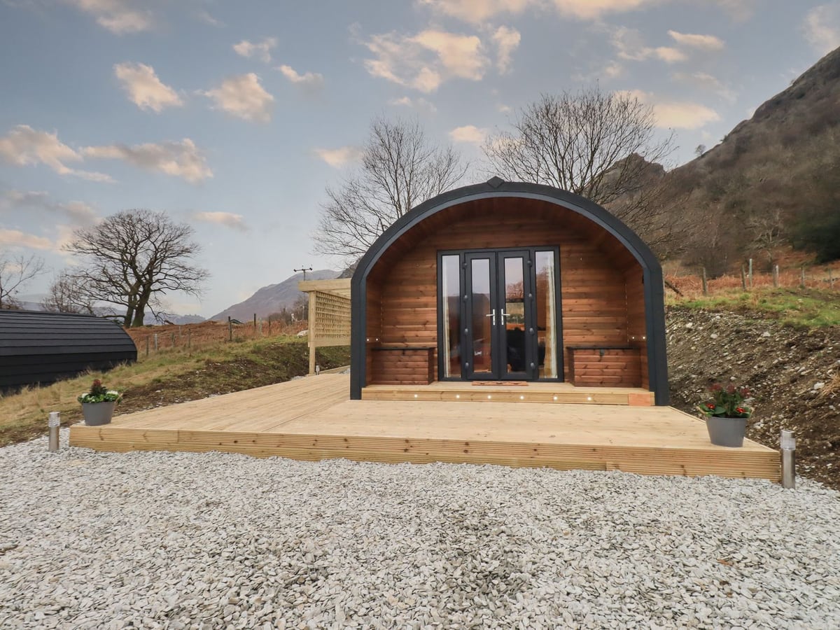 The Stag timber glamping pod with glass doors opening onto a deck beside gravel and a hillside