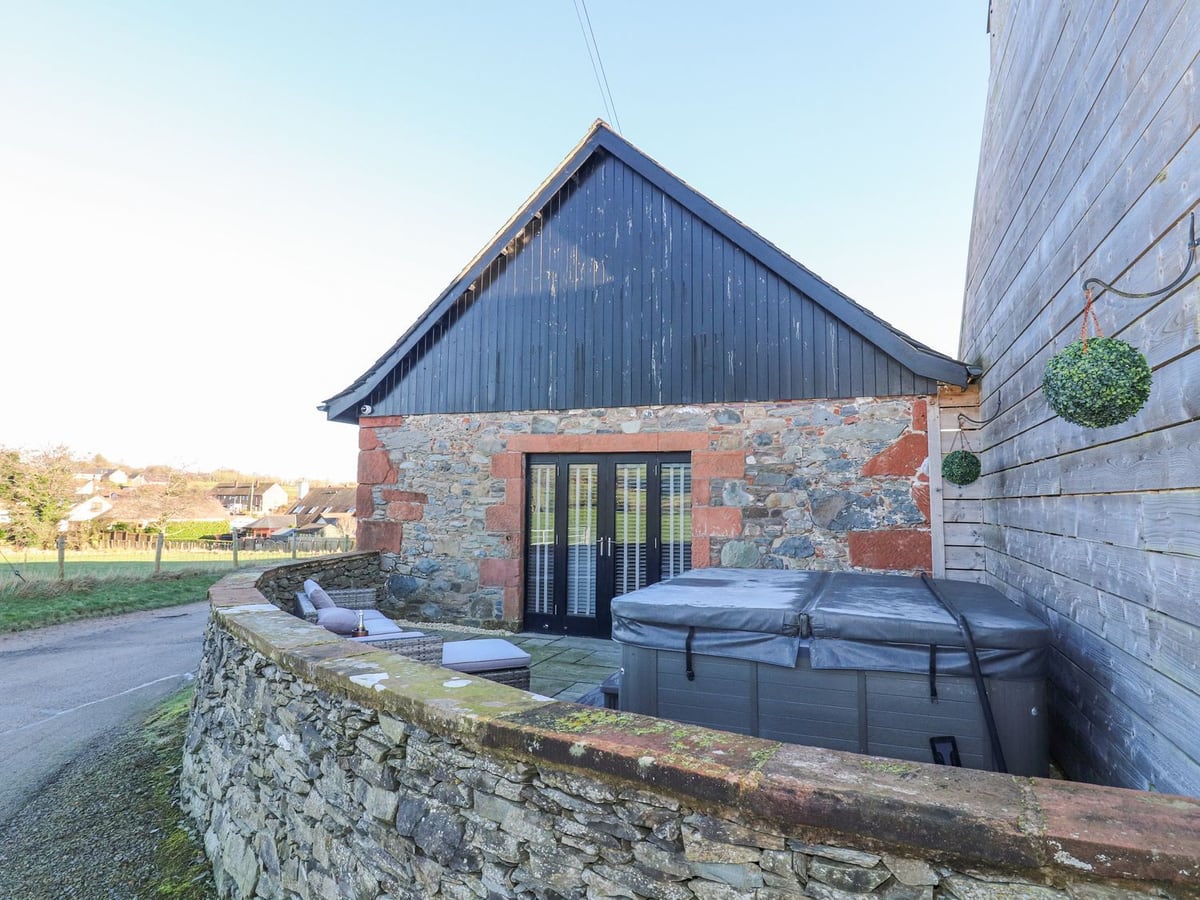 Covered hot tub and outdoor seats behind a low stone wall beside The Steading