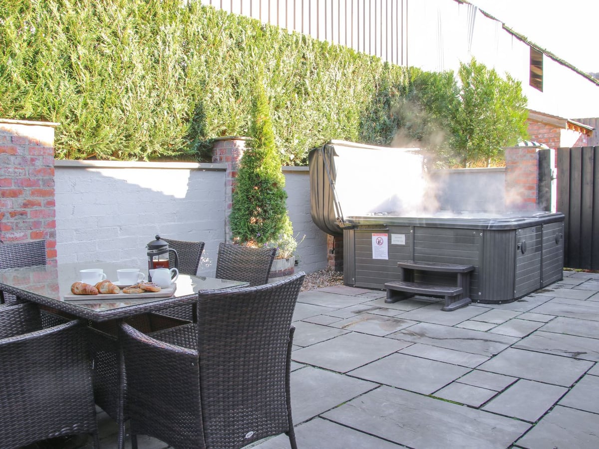 Hot tub and outdoor dining table on The Turnip House's patio, beside a wall and tall hedge