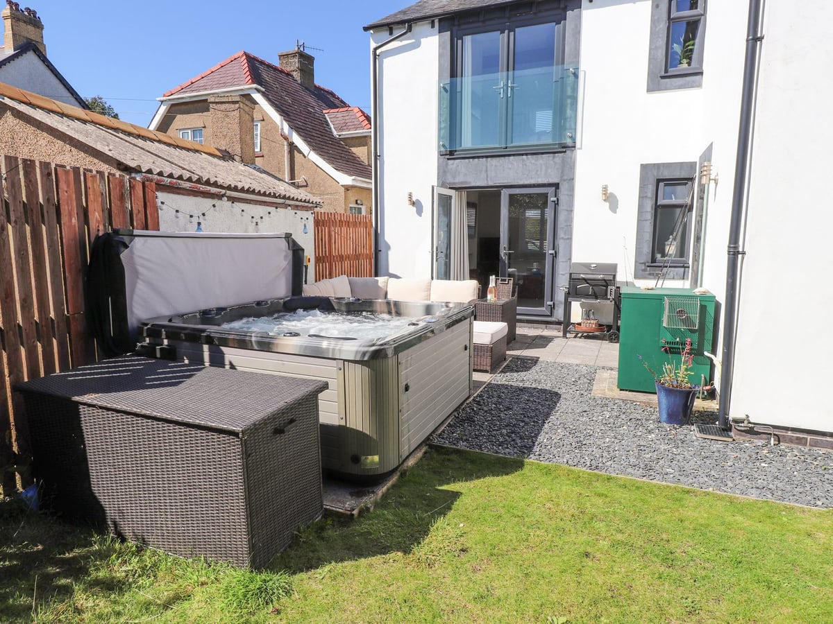 Rear garden at The White House with lawn, open hot tub, wicker sofa and patio doors to the house