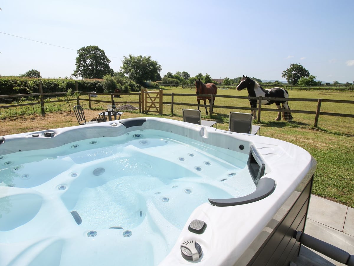 Thimble Cottage's hot tub with garden seats and two horses beyond the post-and-rail fence
