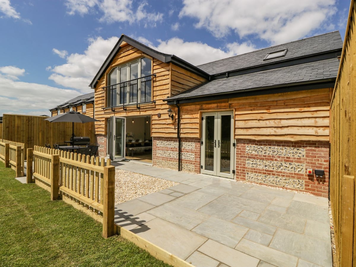 Timber-clad Threshing Barn with a paved patio, picket fence, lawn edge and open glass doors