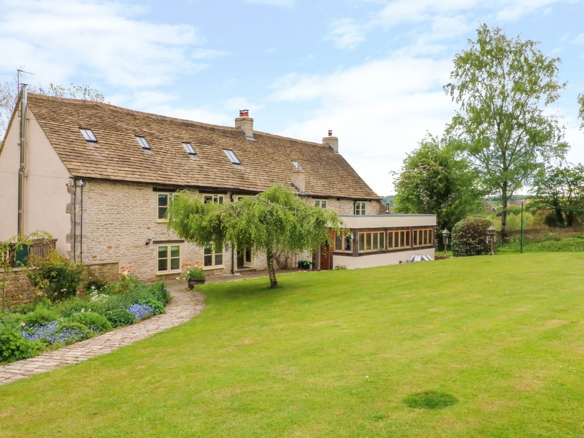 Tickmorend Farm stone farmhouse beside a sloping lawn, trees and a curved stone garden path