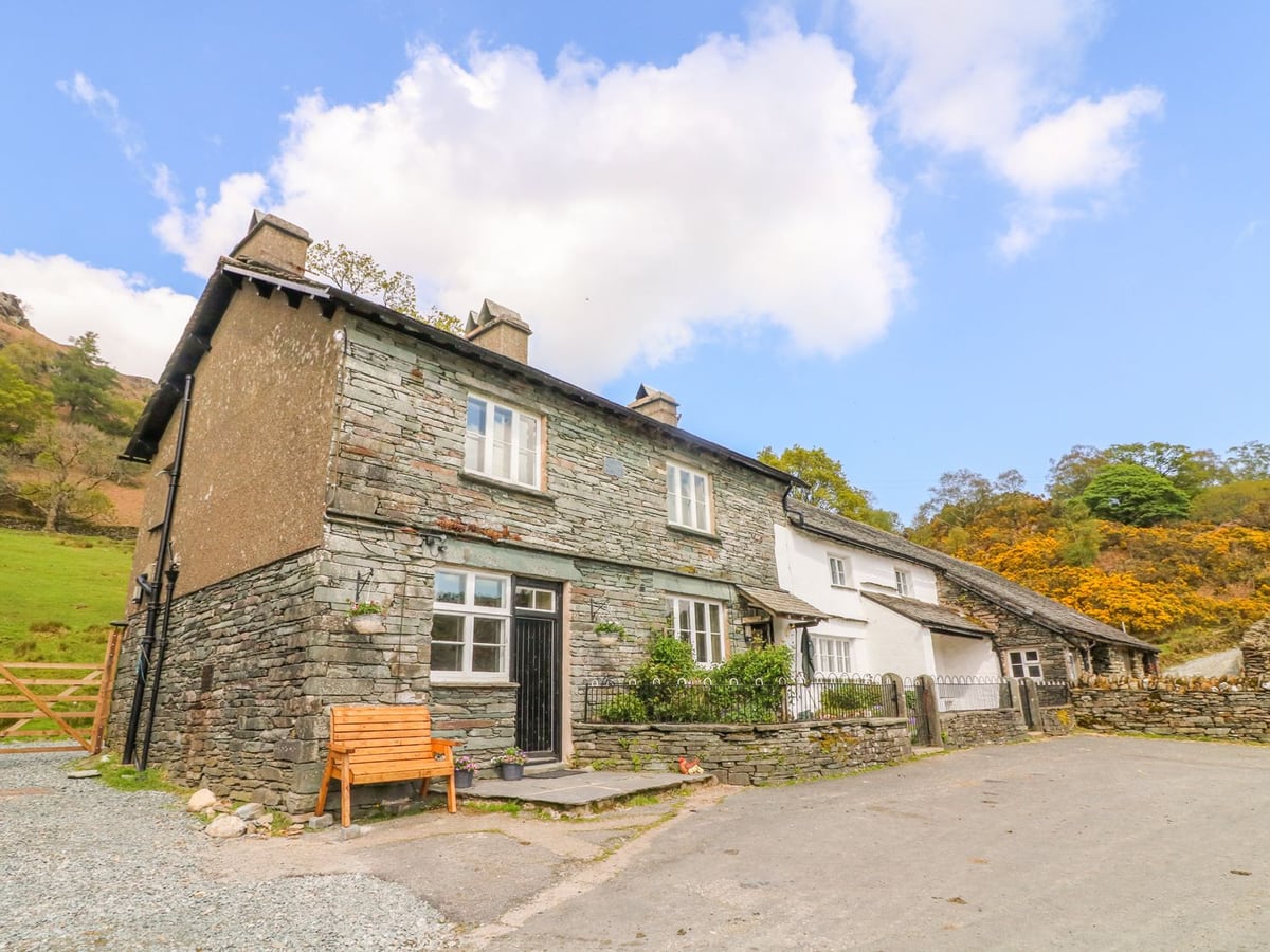 Tilberthwaite Farm Cottage stone frontage with a wooden bench and hillside behind the buildings