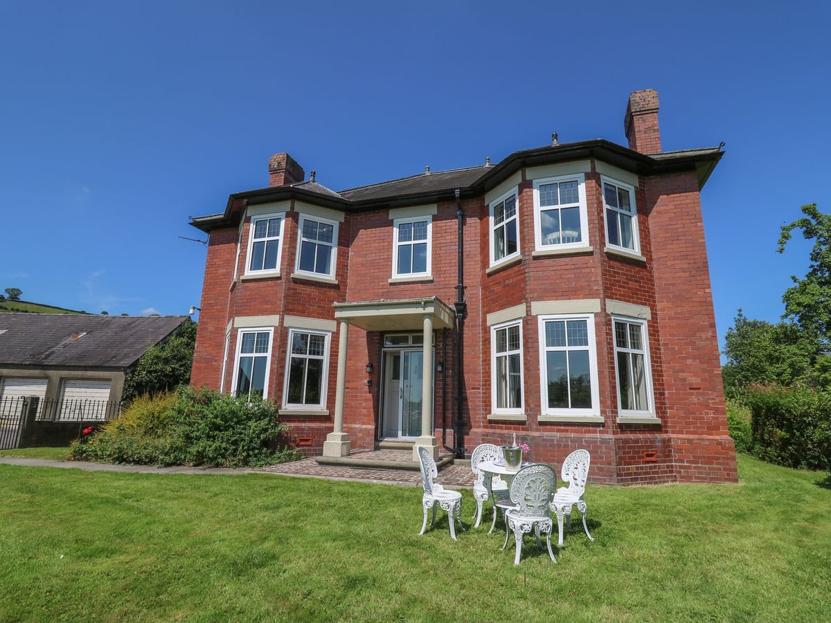 Tirallen red-brick house with a white metal table and four chairs on the lawn outside