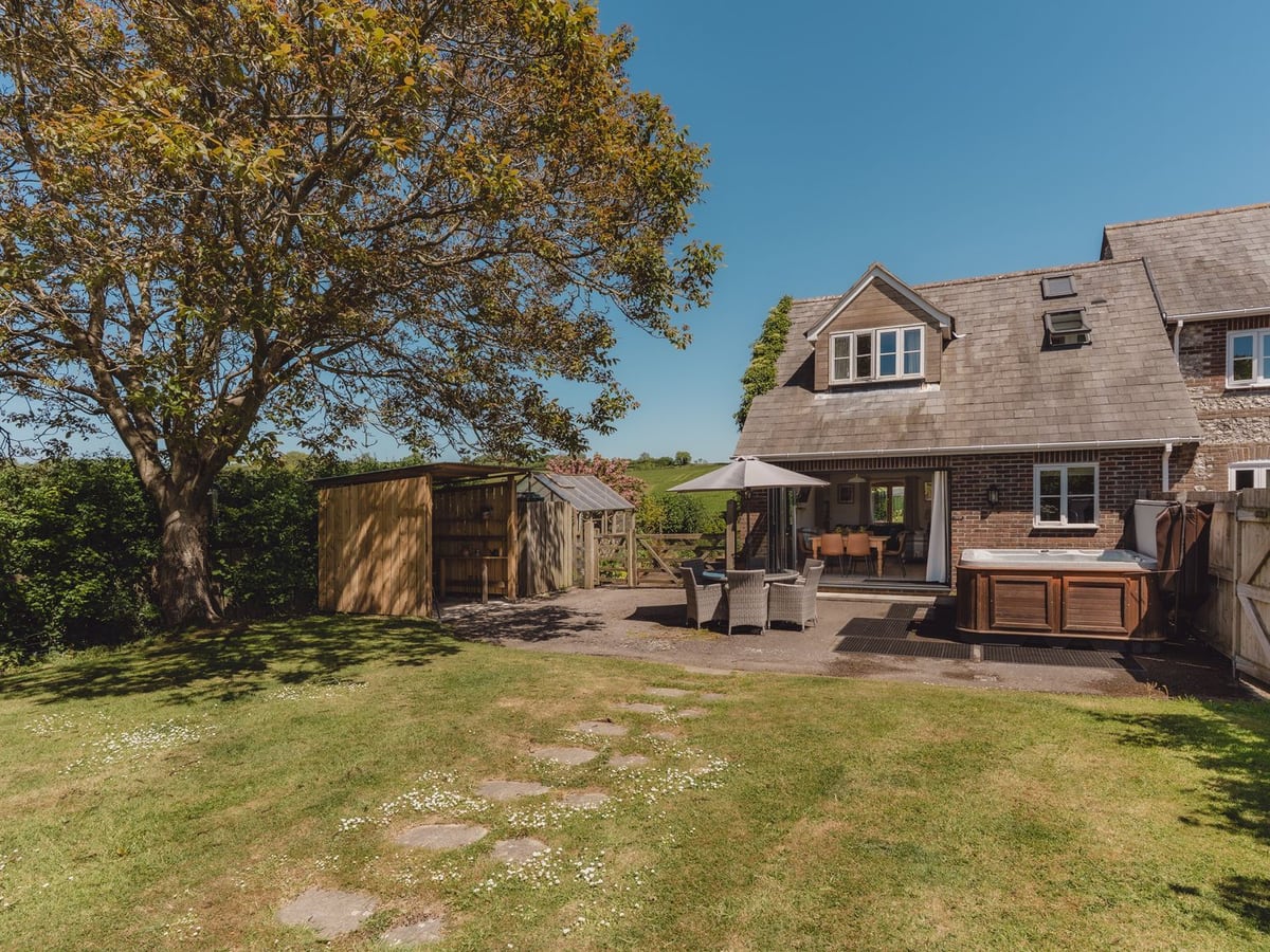 Tokenhill Cottage behind a lawn and patio, with a hot tub, garden table and timber shelter