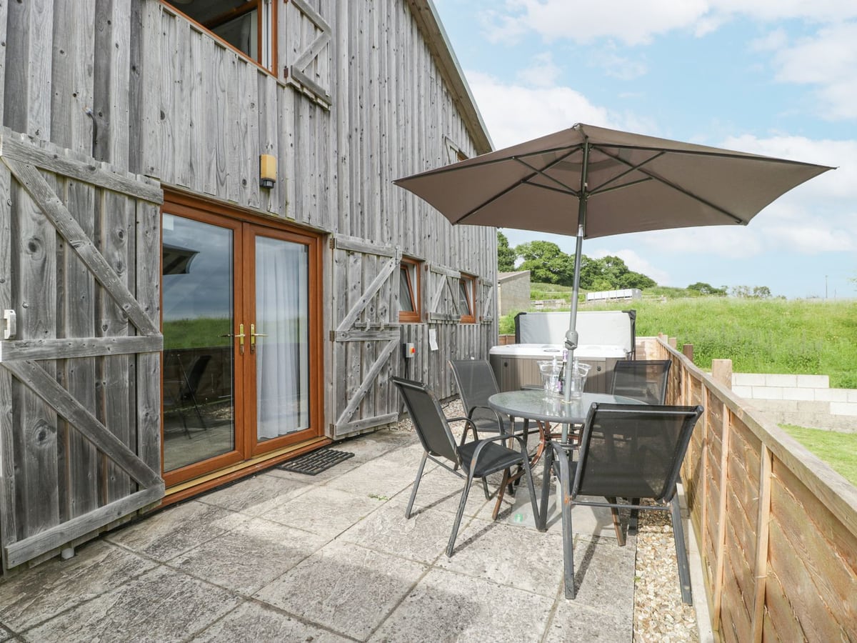 Top Lodge timber barn with a paved patio, table and parasol, a hot tub and a wooden fence beside grass