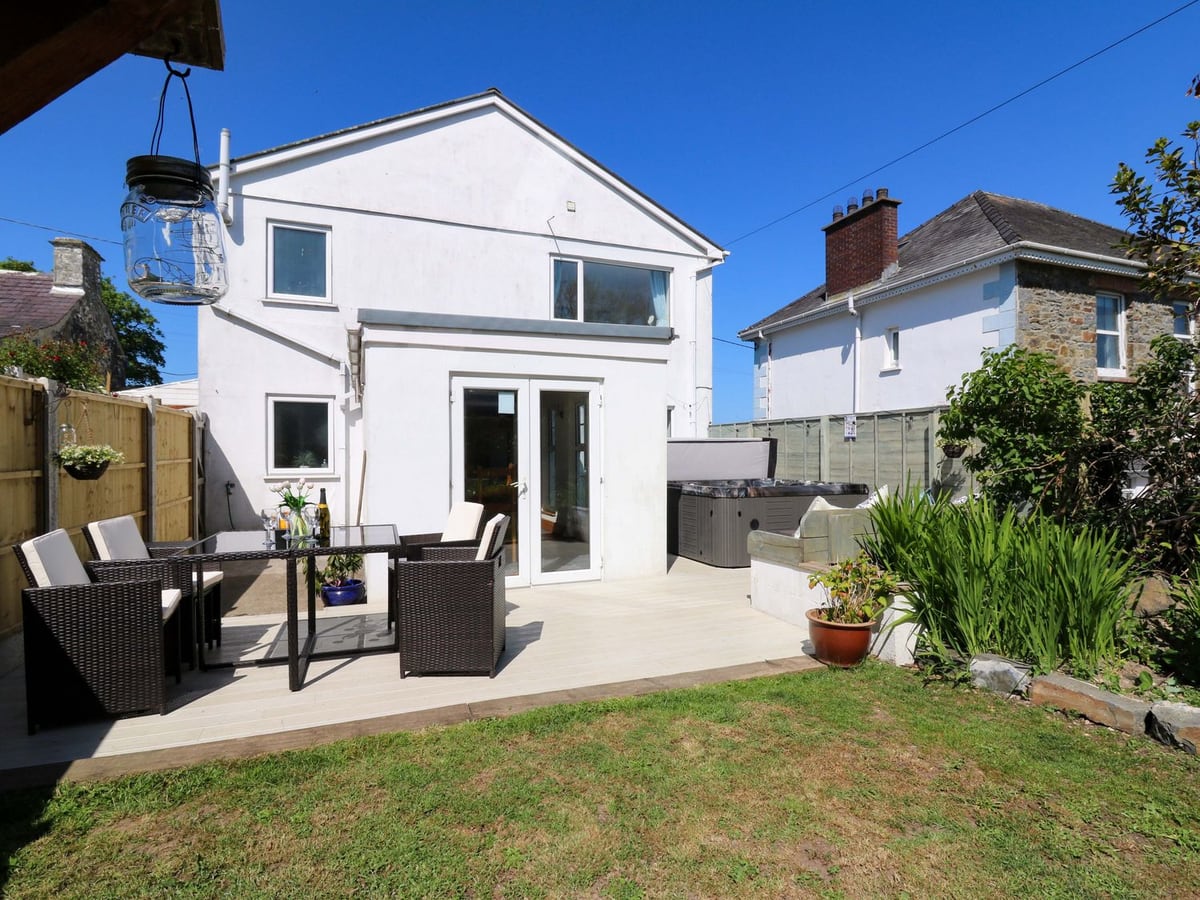 Rear of Towyn Hall with deck, rattan dining set, hot tub with raised lid, lawn and fence