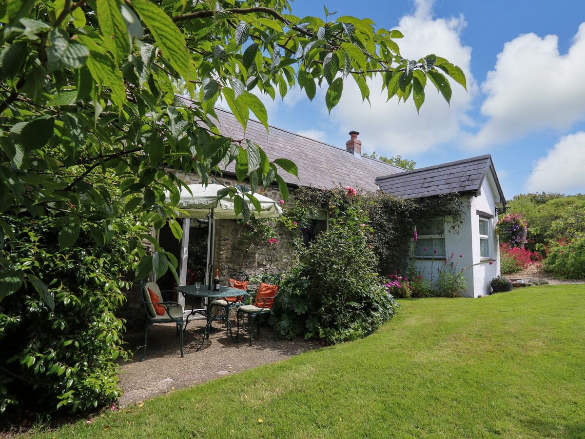 Trawsnant Cottage stone and white cottage with patio table, parasol and a mown lawn