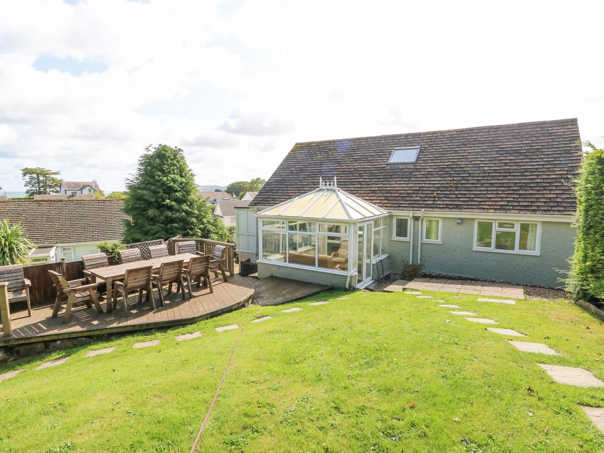 Treestumps rear exterior with conservatory, lawn and a raised deck with outdoor dining chairs