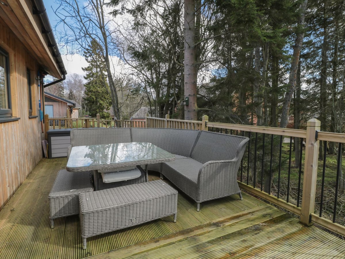 Woodland-facing deck at Treetops with grey corner seating beside the timber lodge.