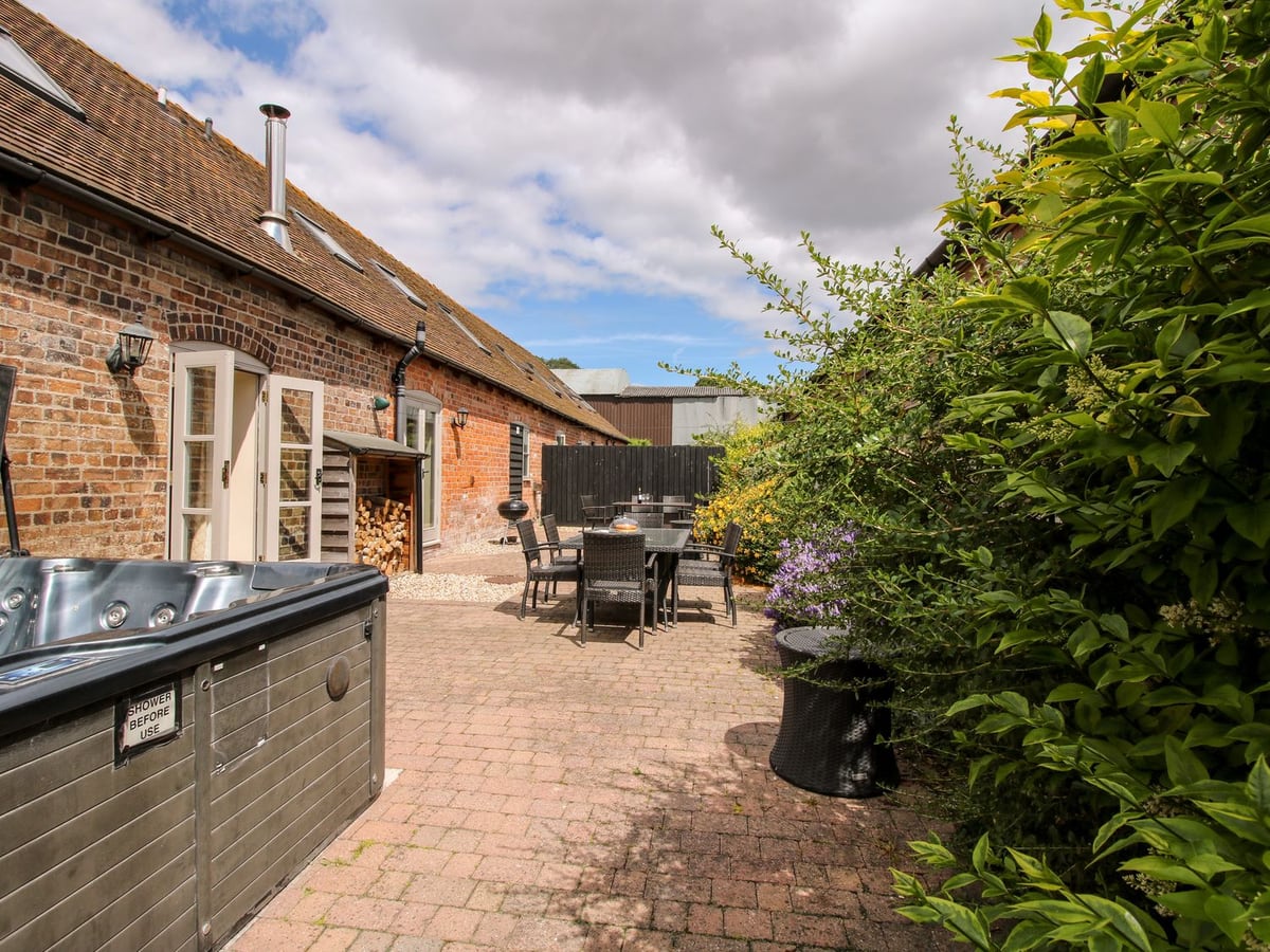 Trooper's Barn's brick rear wall beside a long patio with a hot tub and dining tables