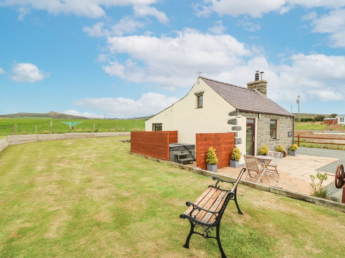 Ty Bach Ysgo cottage with a lawn, bench, patio table and chairs, and a screened hot tub with its lid on