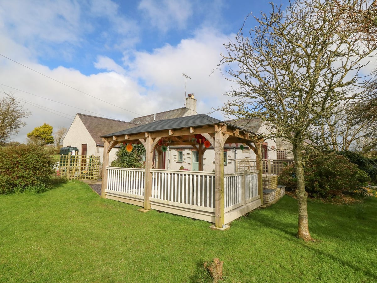 Ty Gwennol cottage and garden with lawn, trees and a wooden gazebo beside the house