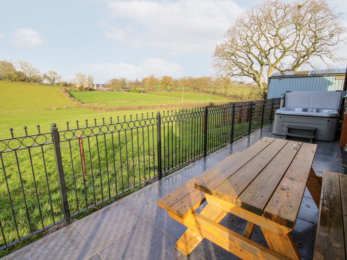 Ty Gwyn patio with a picnic bench, railings and hot tub, looking over green fields and bare trees