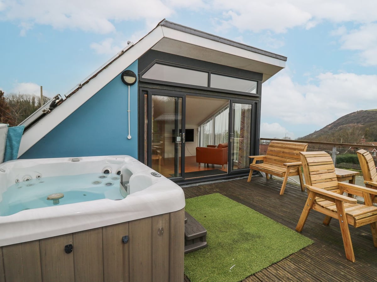 Ty Henri raised deck with hot tub, wooden chairs and glass doors, with a green hill beyond