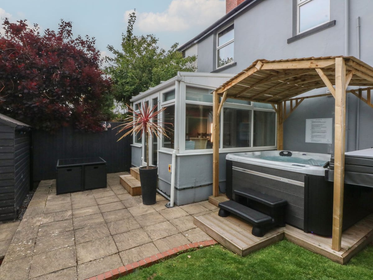 Rear patio and lawn at Ty Llwyd with an open hot tub under a wooden gazebo by the conservatory