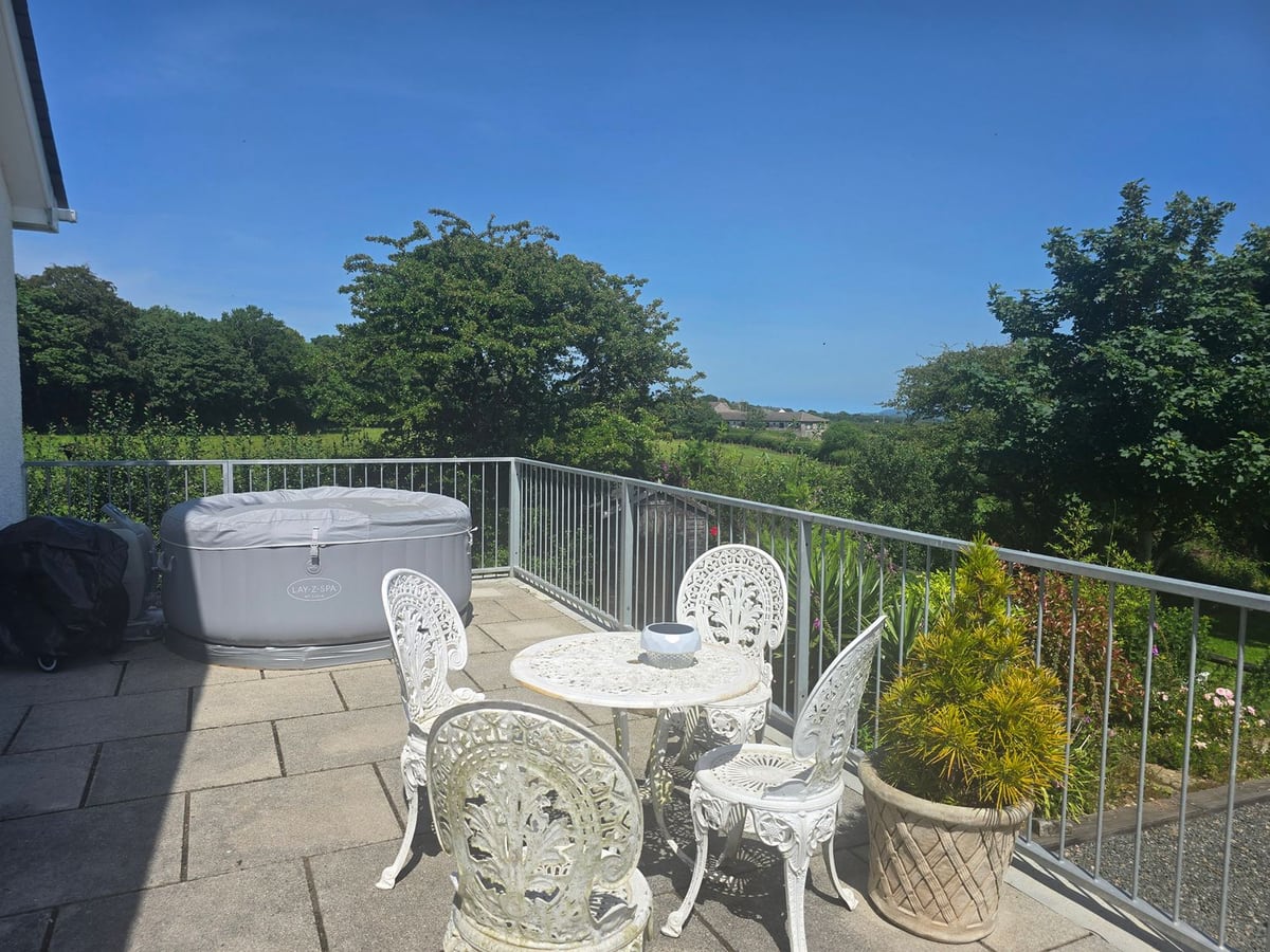 Ty Nain balcony with an inflatable hot tub with its lid on, white metal table and chairs, railings and trees