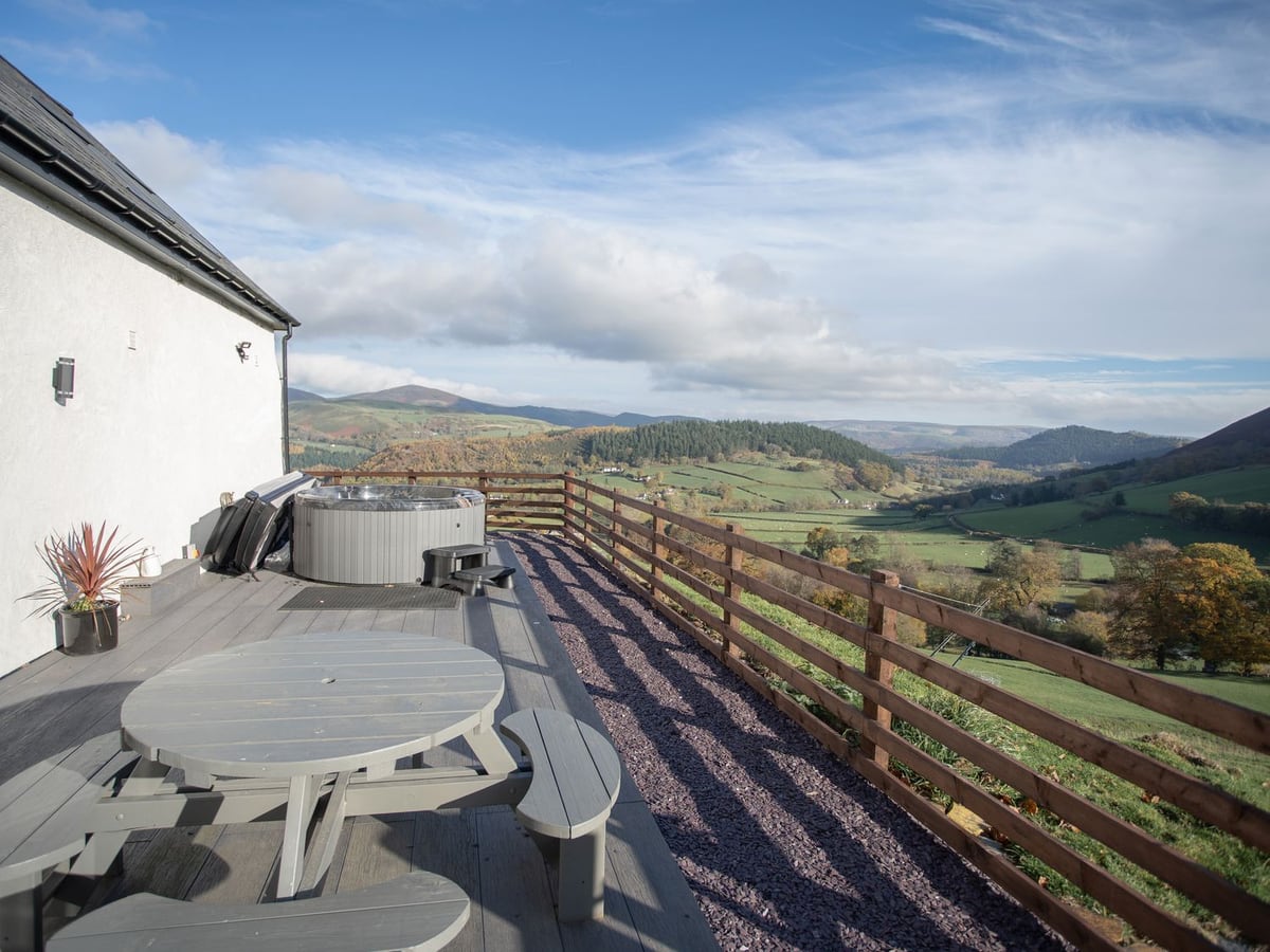 Tyn Llwyn Barn decking with hot tub and picnic table alongside the barn wall, rail fence and valley view