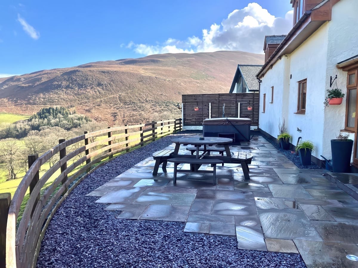Flagstone patio at Tyn Llwyn with picnic table, hot tub, rail fence and a hillside view beyond