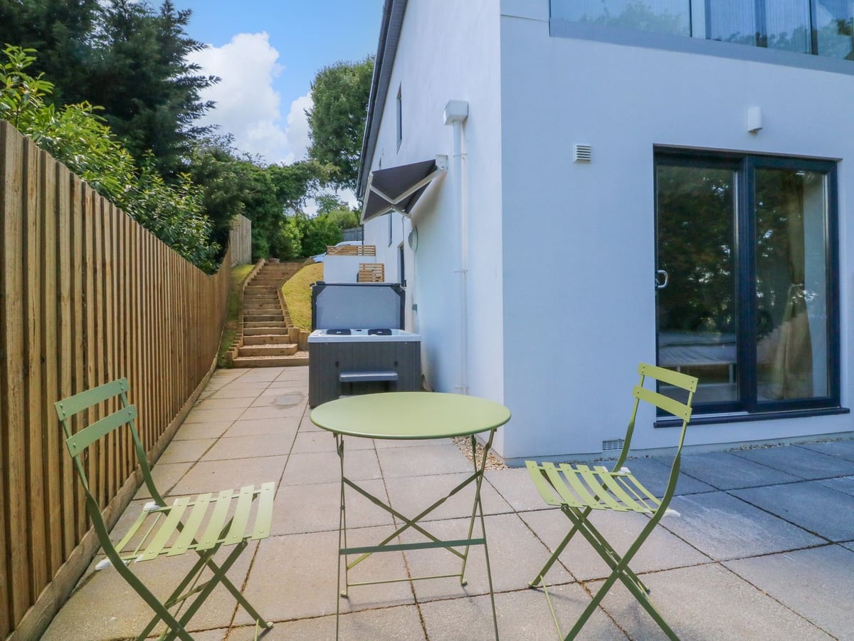 Green bistro chairs on a paved patio beside Valise, with a hot tub and garden steps