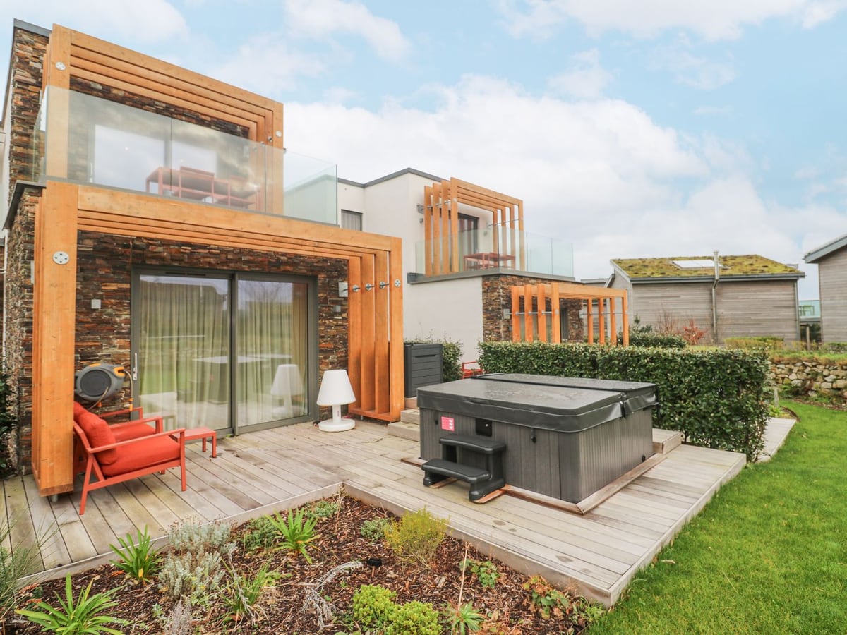 Villa 80's stone exterior, timber-framed balcony and deck with a covered hot tub and red chair